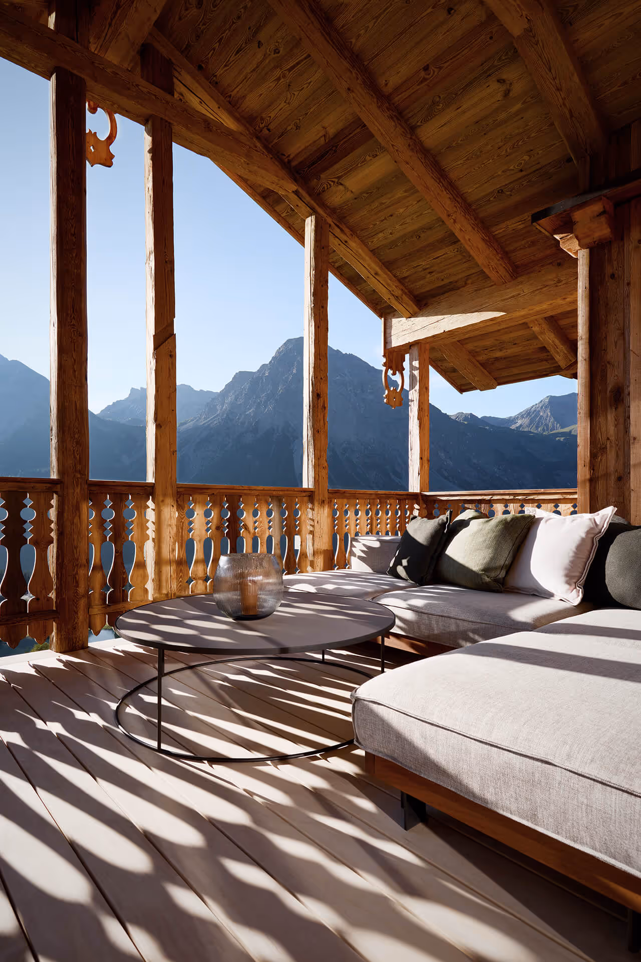 Holzbalkon mit gemütlicher Sitzgruppe und Blick auf bergige Landschaft bei klarem Himmel.