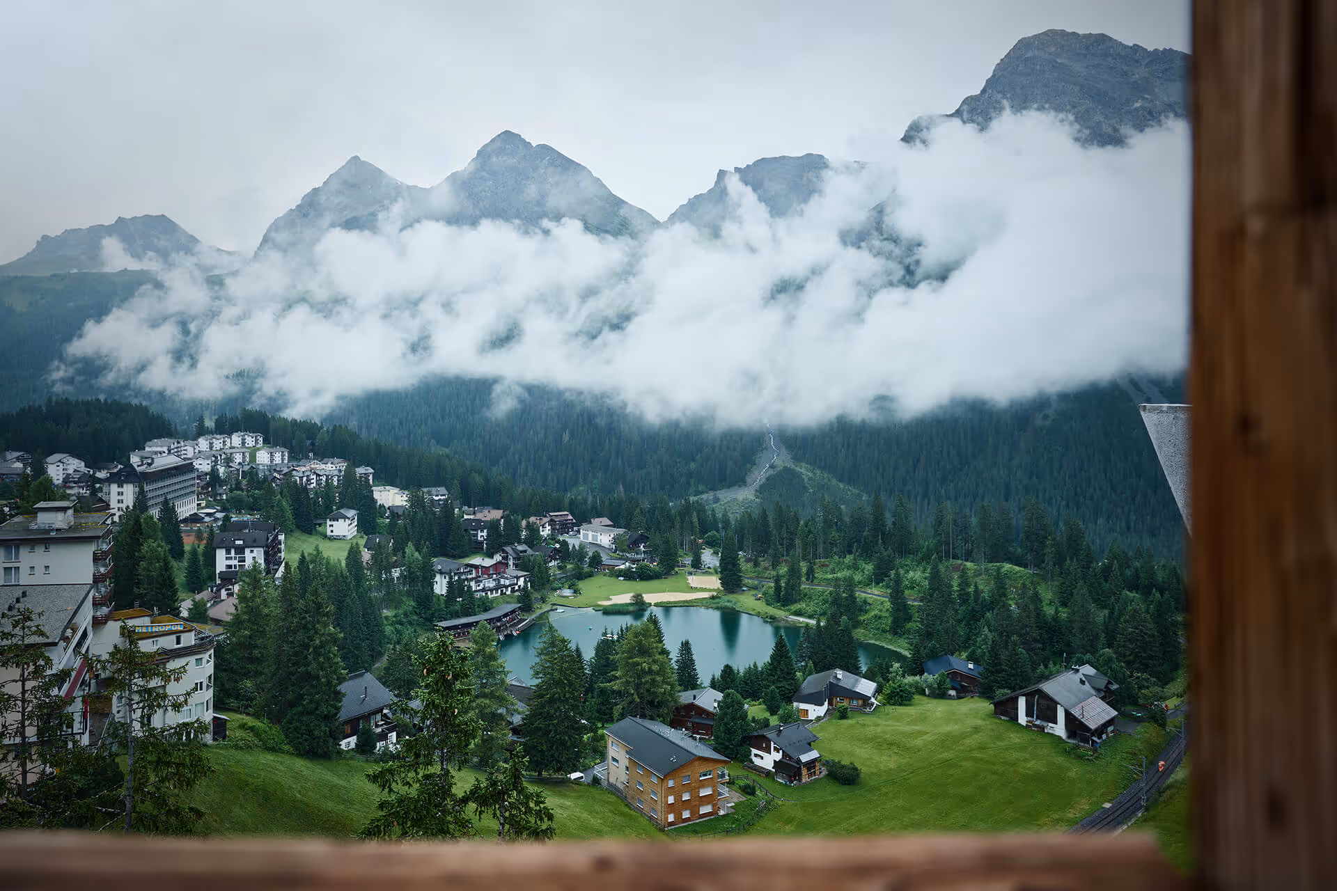 Blick aus dem Chalet auf einen kleinen See, grünen Wiesen und Nadelwäldern.