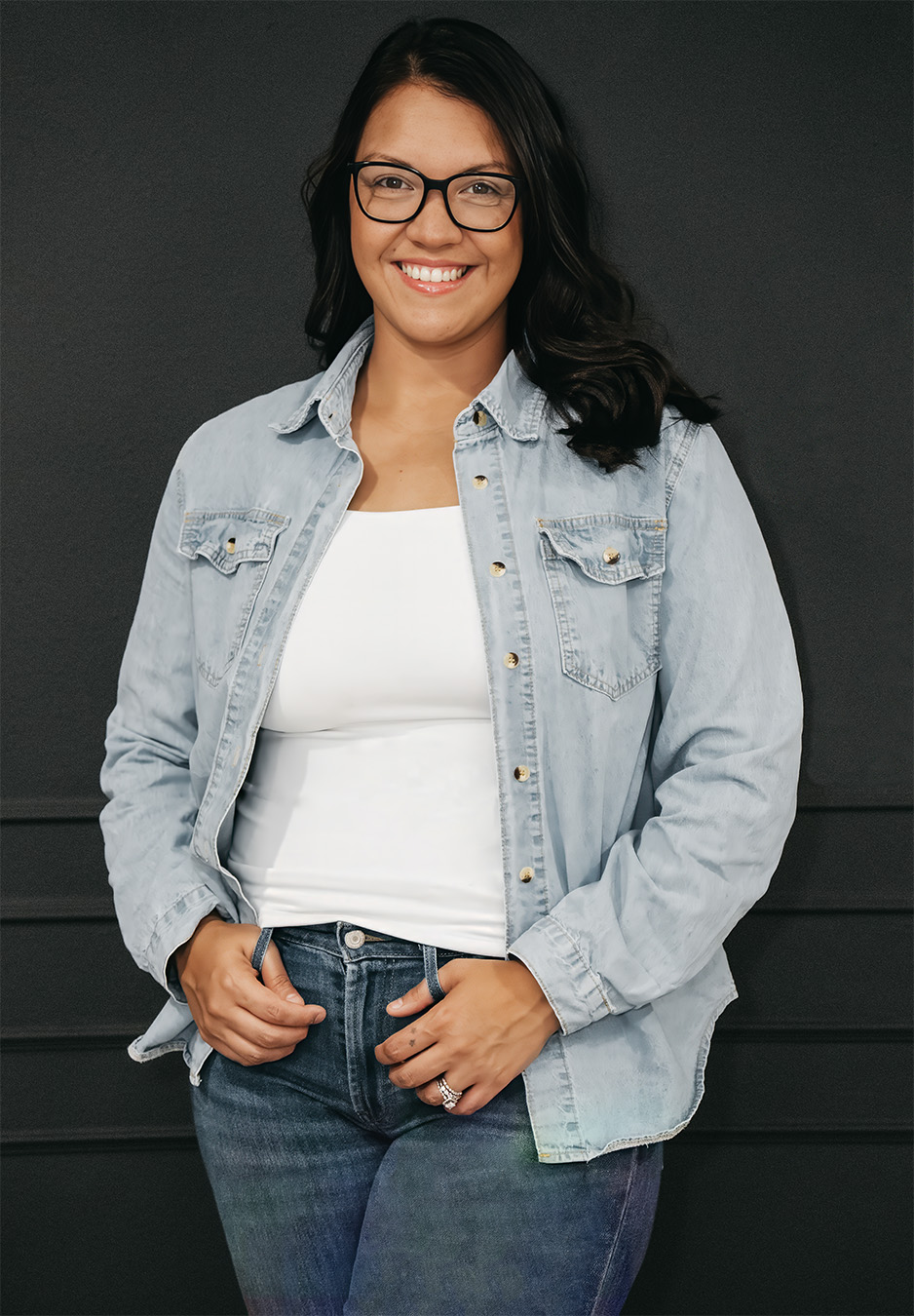 A young female that works for Shutterpix Photography as a professional wedding, portrait, boudoir, family photographer wearing a blue denim shirt and jeans.