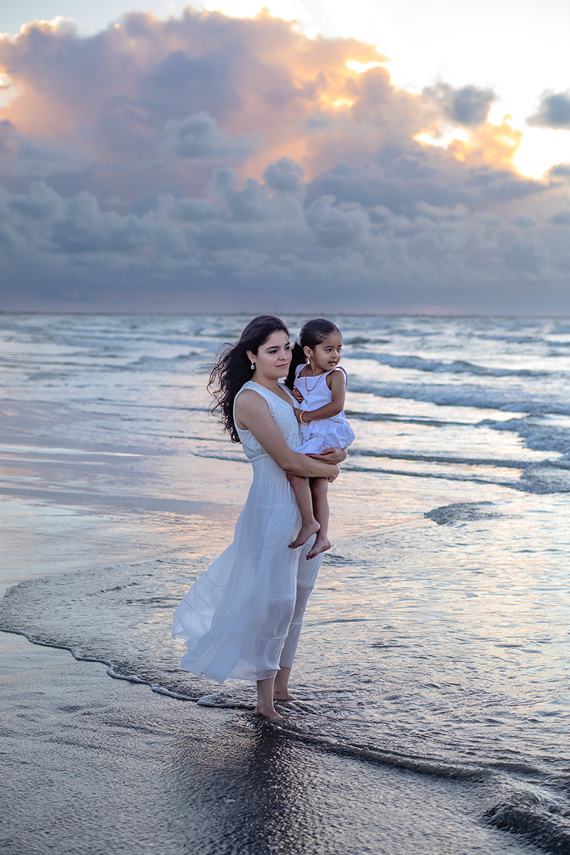 A mother holding her daughter over the beautiful ocean.
