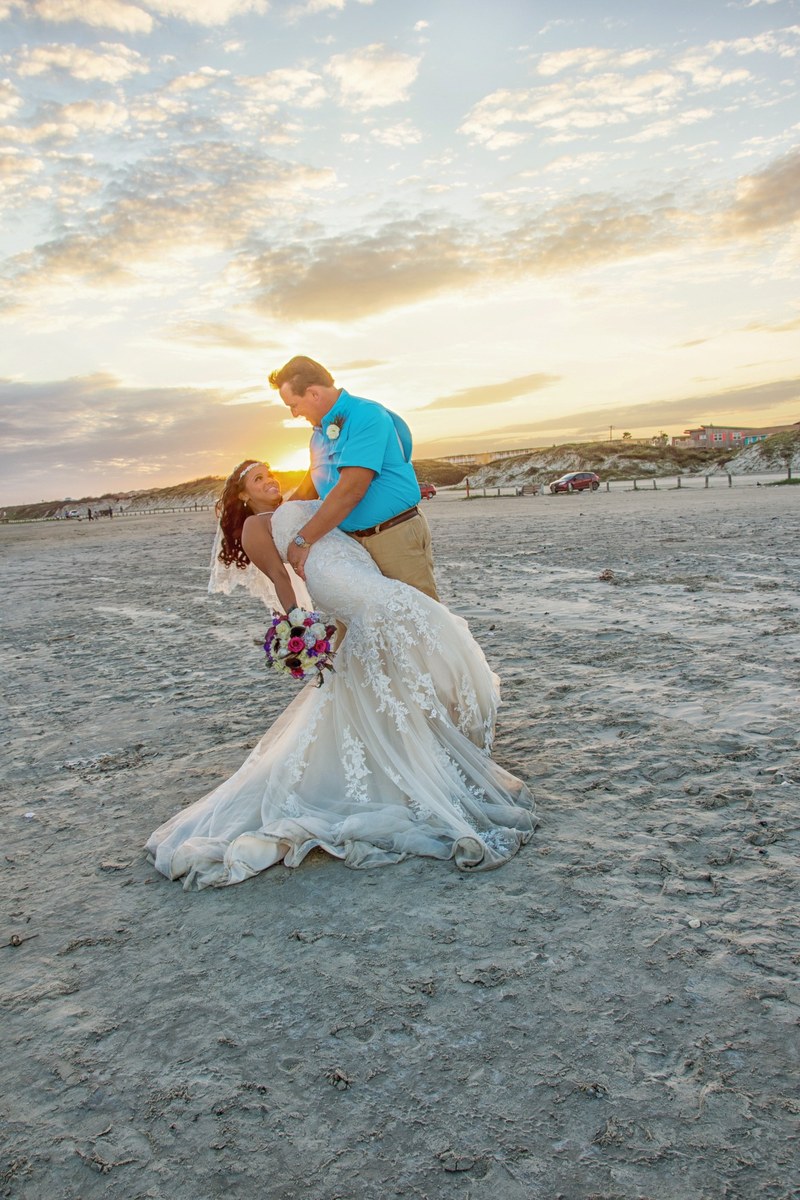 A Couple On the Port Aransas Beach posing in the dip with a beautiful wedding dress and the sun setting in the dunes. 