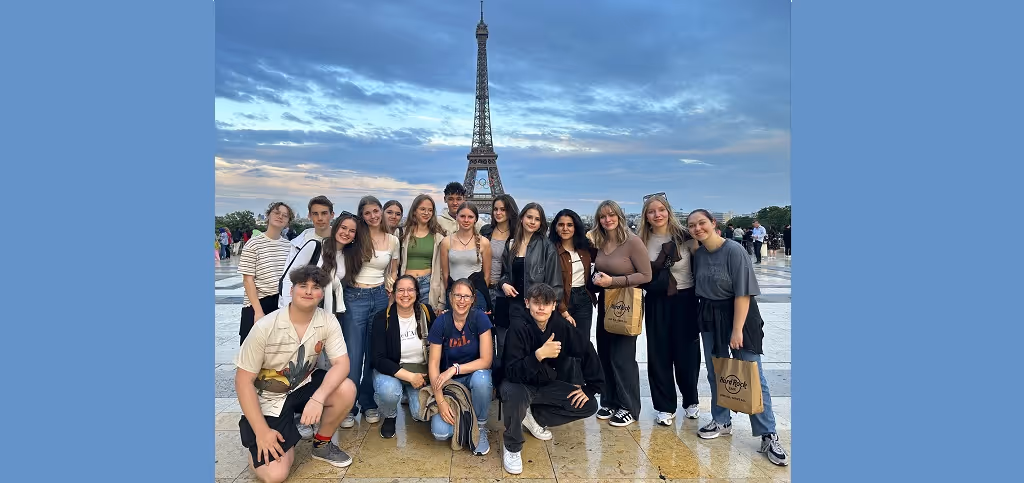 Gruppe Jugendlicher posiert vor dem Eiffelturm in Paris bei wolkigem Himmel. Das Bild zeigt einen Ausschnitt unserer Exkursion nach Paris.