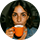 Femme souriante tenant une tasse de café orange, assise devant un fond flou.