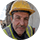 Portrait d'un homme avec un casque jaune de chantier, souriant, sur un fond clair.