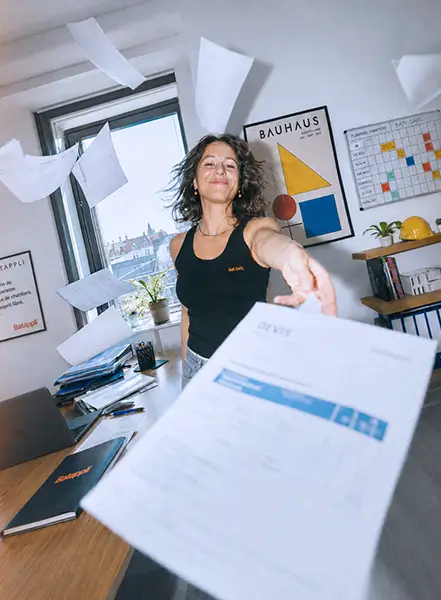 Une femme souriante lance un devis en l'air dans un bureau lumineux et moderne.