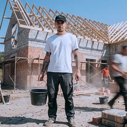 Facadier portant un seau sur un chantier devant une maison en construction.