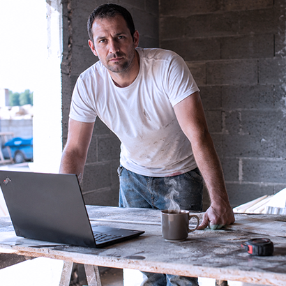 Artisan chauffagiste penché sur une table de chantier avec un ordinateur portable et une tasse fumante.