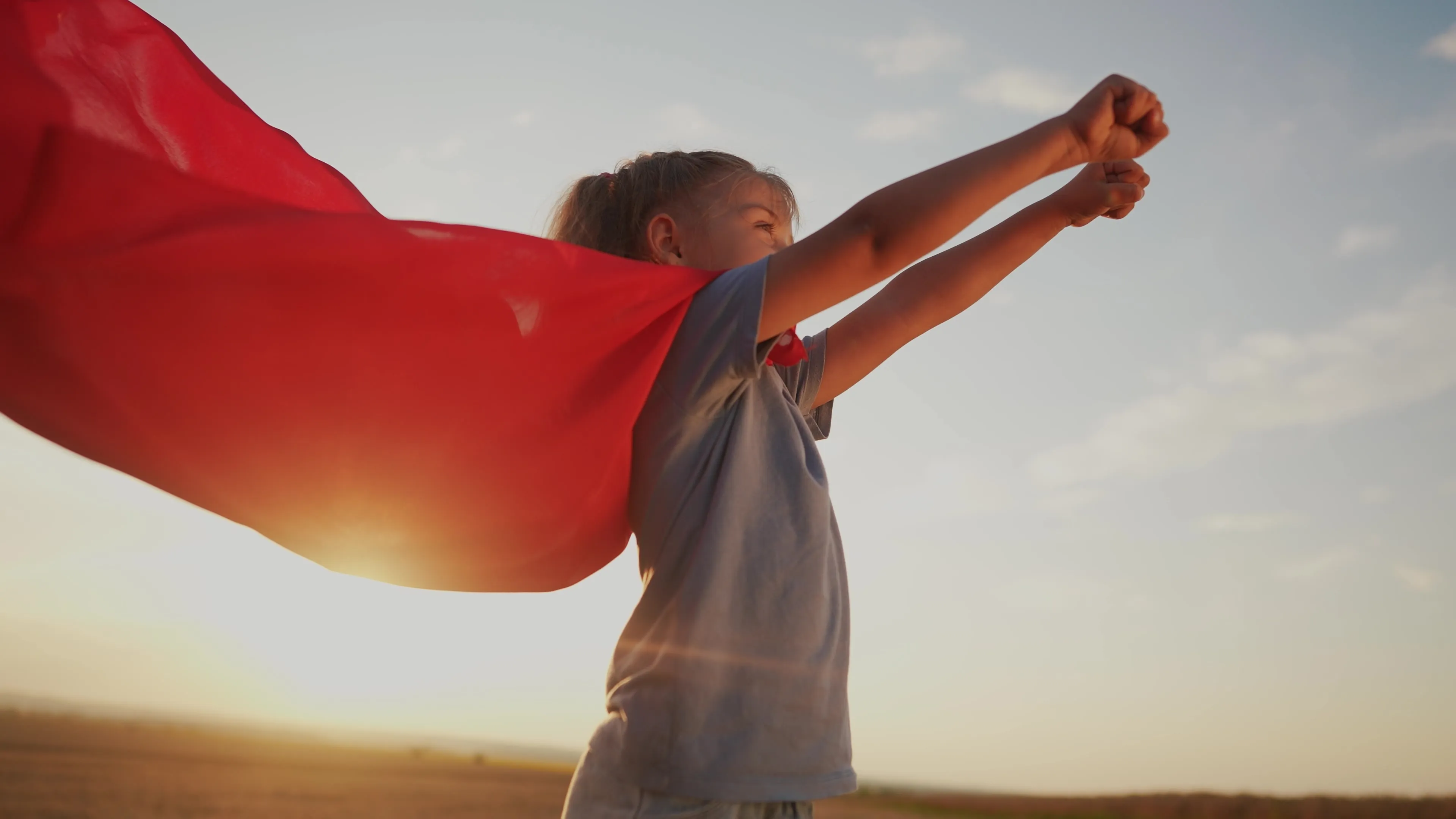 girl with the cloak. concept of happy childhood and family for a child. little girl in a superhero costume stretched hand forward, a lifestyle red cape and a blue T-shirt, sunset on the background