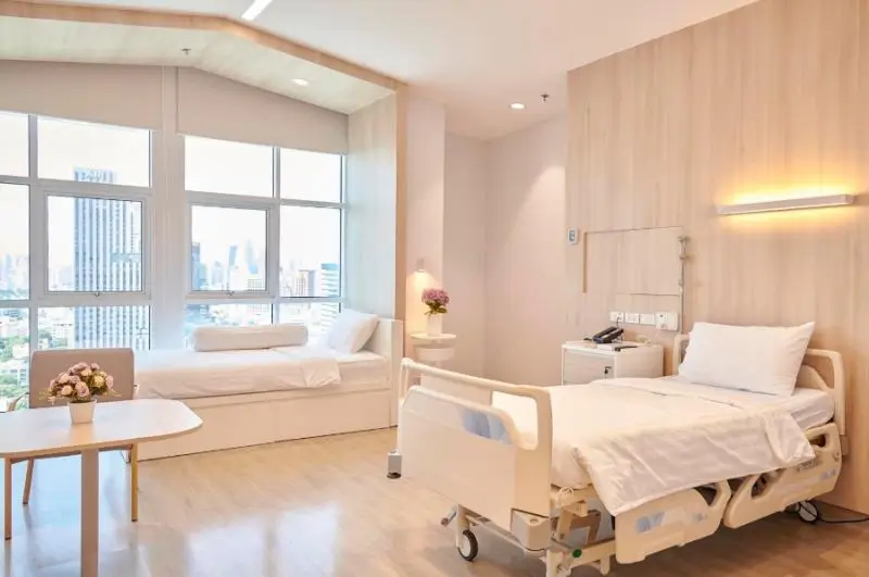 Bright hospital room with patient bed and sofa by large window