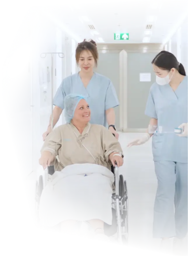 Smiling patient in wheelchair being escorted by two nurses in hospital hallway