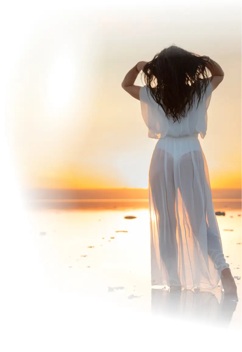 Woman in white dress at sunset with arms raised