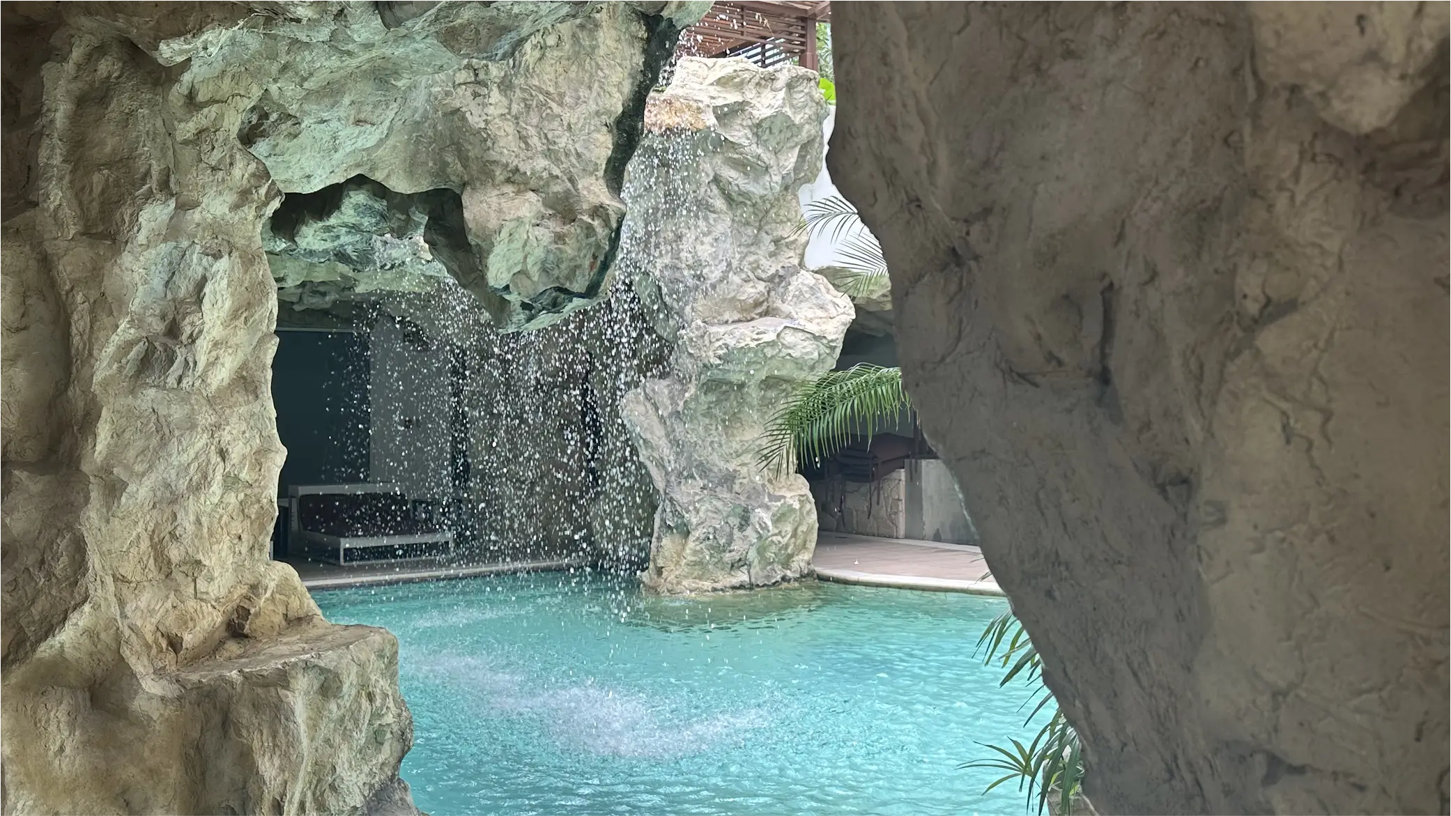 Rock cave waterfall flowing into a turquoise swimming pool.