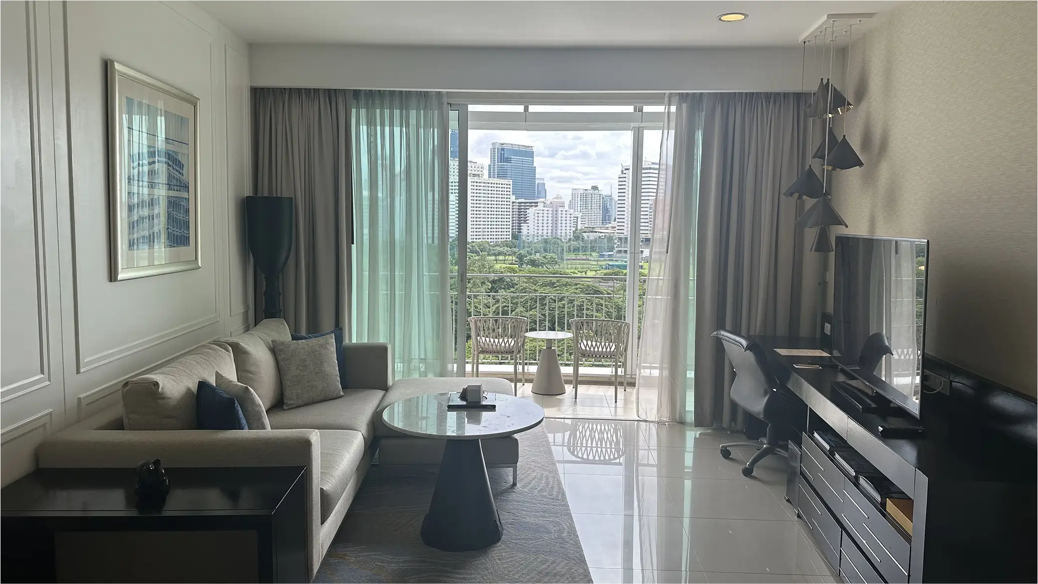 Bright living room with sofa, TV, and balcony overlooking Bangkok skyline.