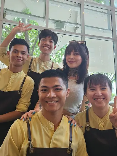 A woman poses with four smiling restaurant staff members wearing yellow shirts and brown aprons.