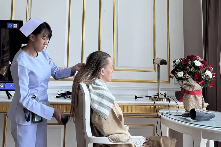 Nurse blow-drying a patient’s hair in a well-decorated recovery room.