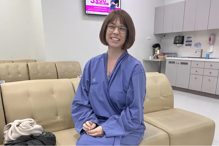Woman in a hospital gown smiling while sitting in a clinic waiting area.