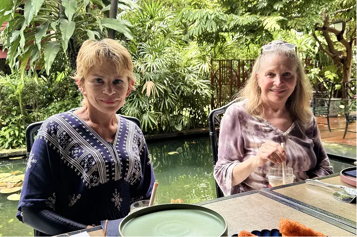 Two women enjoying a meal at an outdoor restaurant surrounded by greenery.