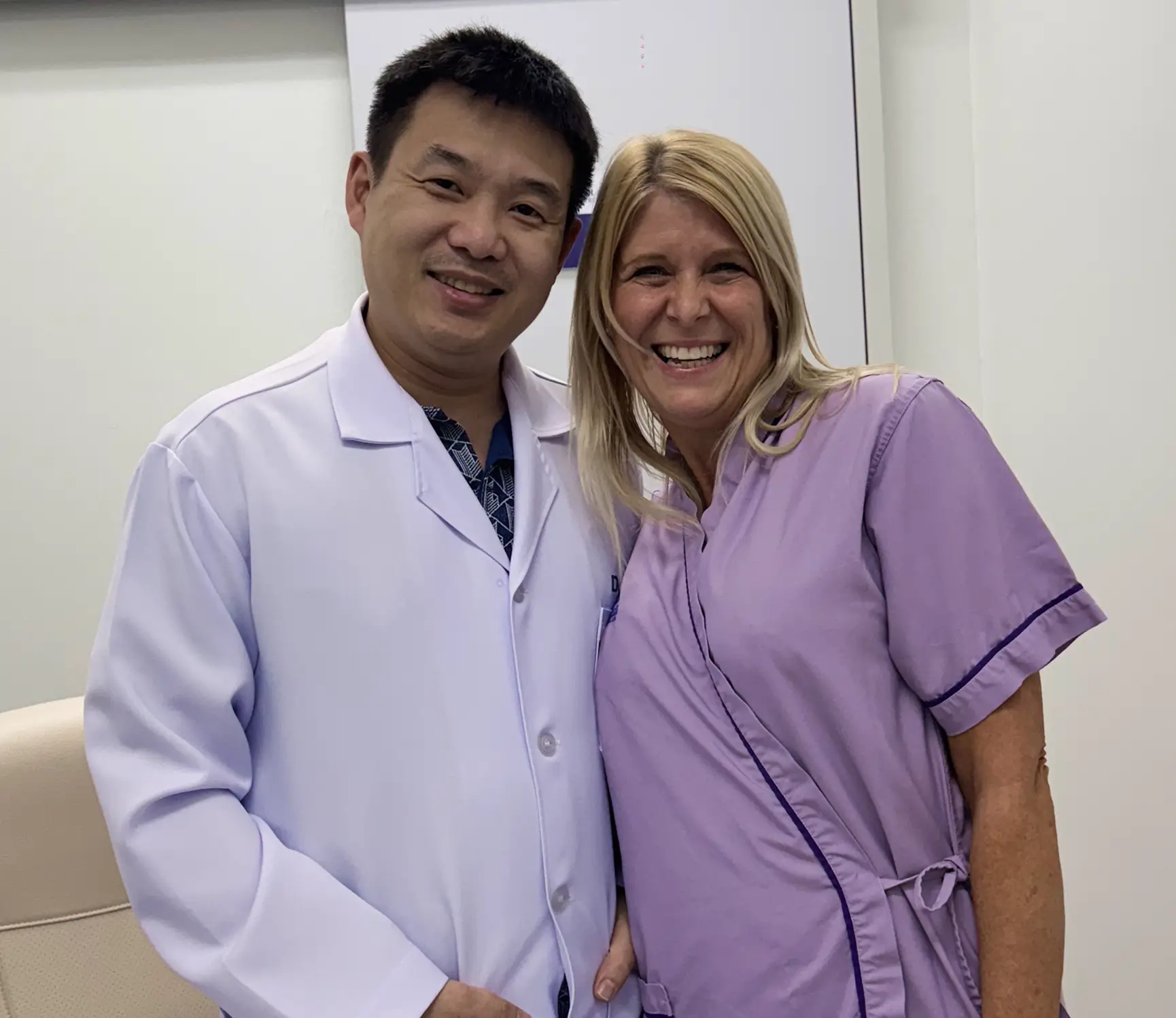 Smiling male doctor in white coat standing next to a smiling woman in a purple medical gown.