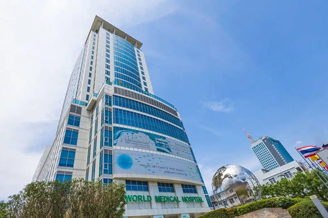 Tall modern building of World Medical Hospital with glass windows under a blue sky and a large metallic globe sculpture in front.