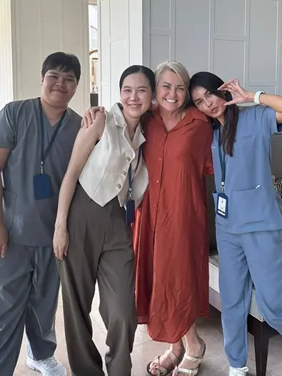 Four smiling adults posing indoors; two in medical scrubs, one in a sleeveless top, and one in a rust dress.