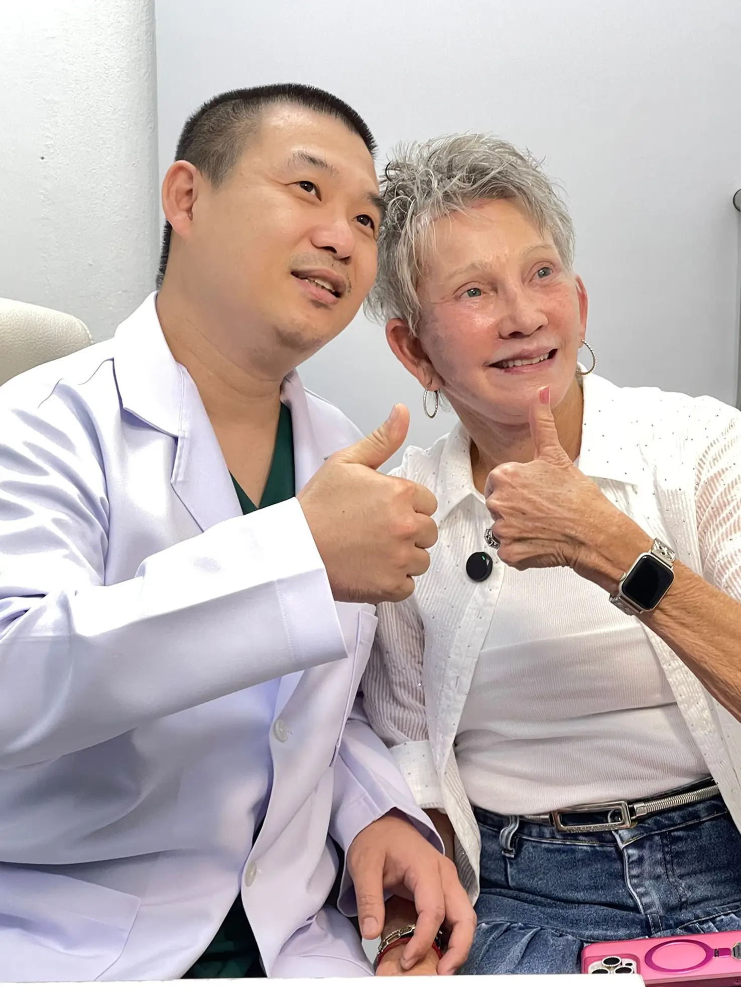 Patient in bed forming a heart shape with her hands beside a smiling nurse.