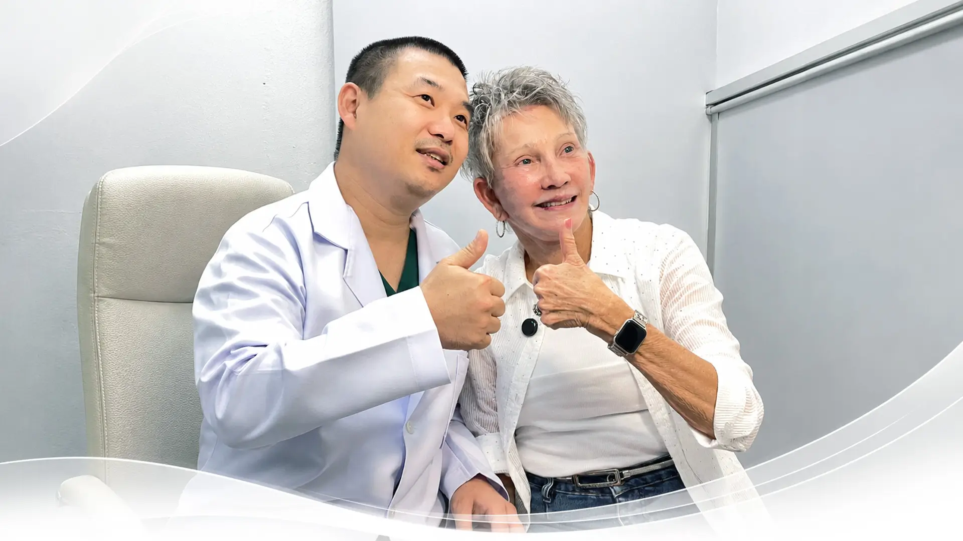Doctor and elderly woman smiling and showing thumbs up together in a medical office.