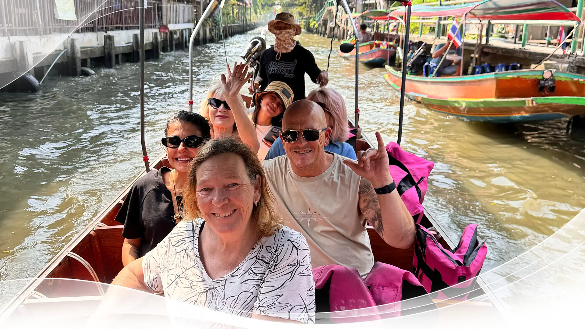 Group of tourists smiling and waving on a boat tour through a canal with another boat nearby.