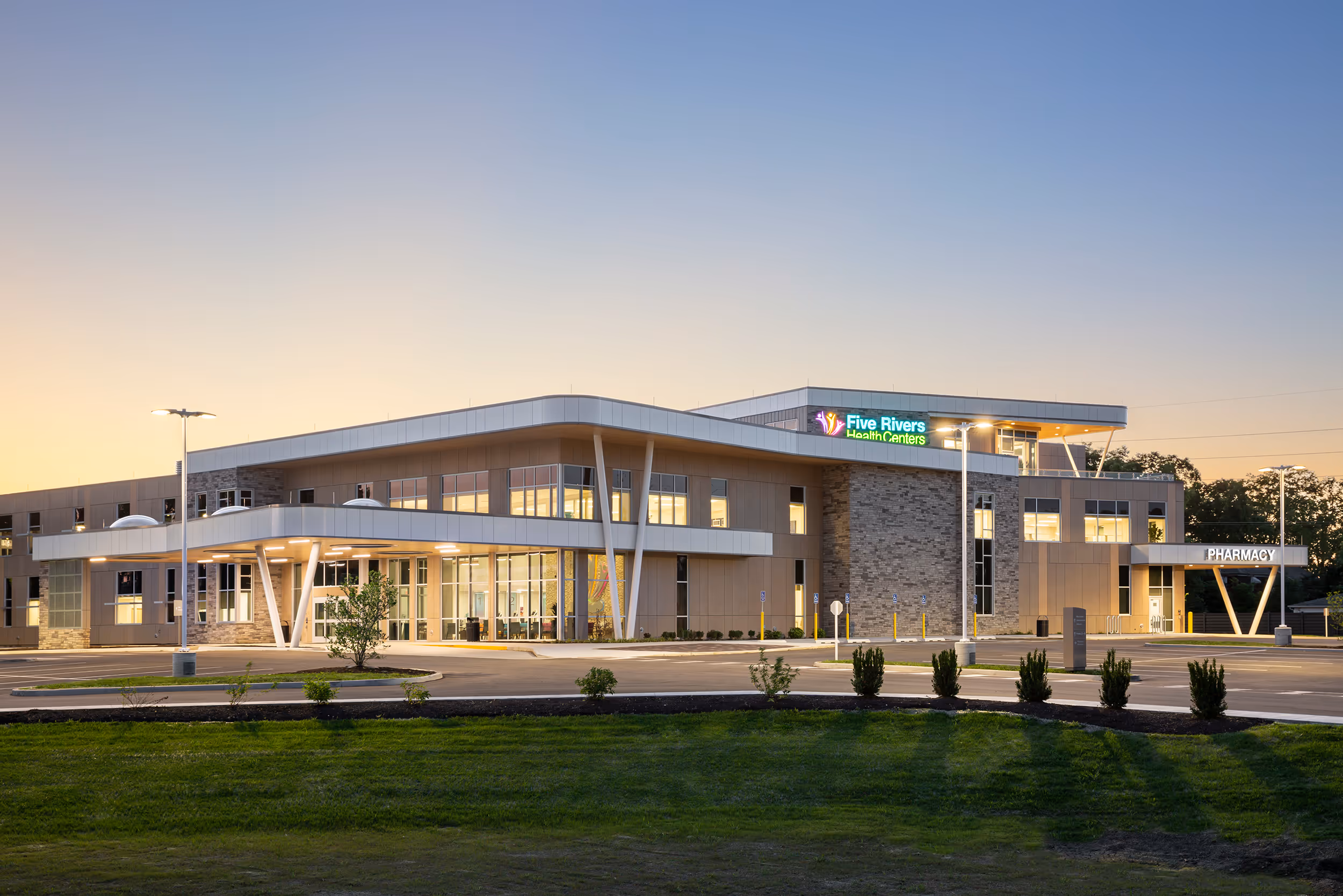 Modern Two-story Five Rivers Health Centers building with illuminated signage and pharmacy entrance at dusk.
