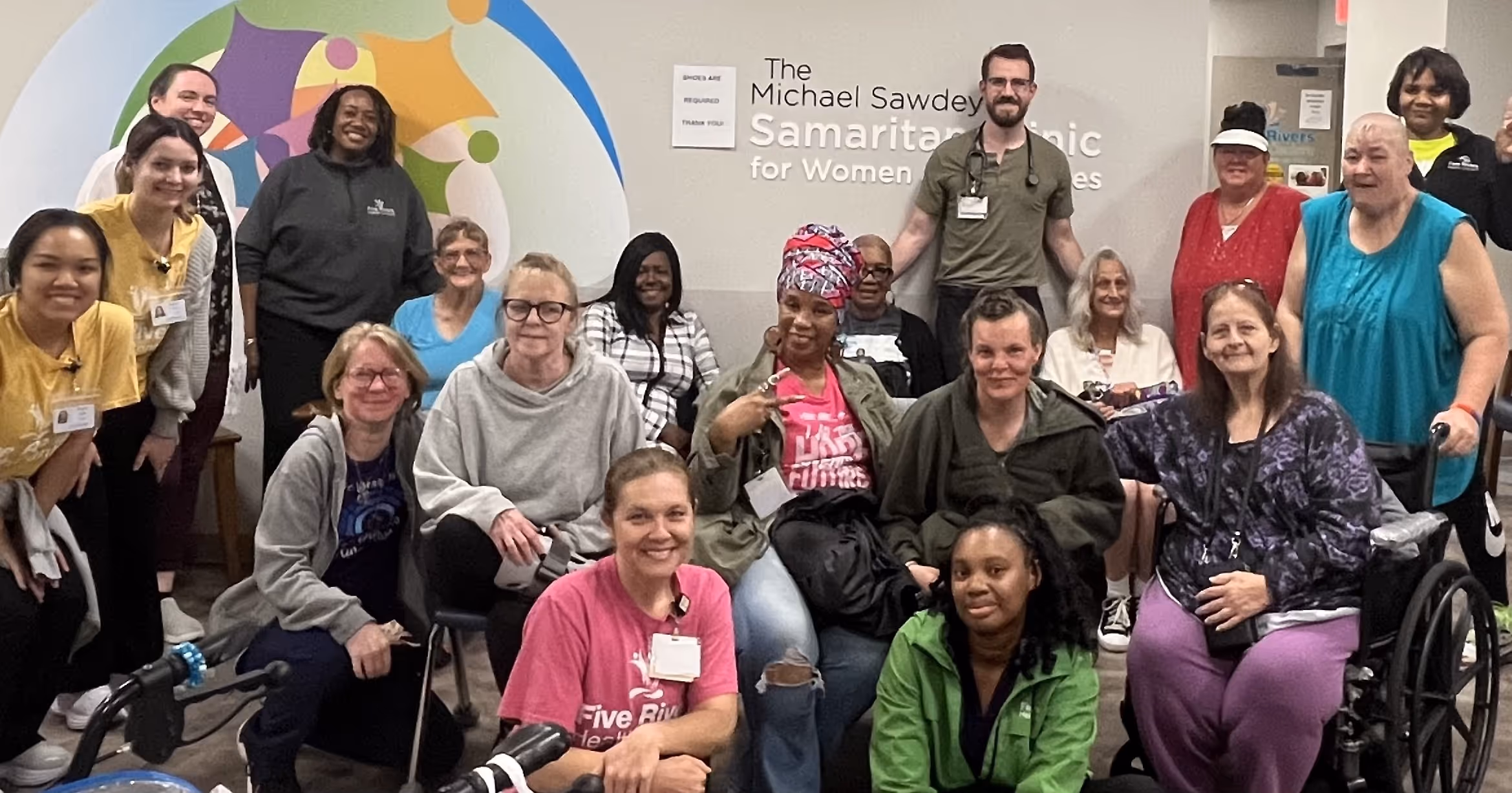 Group of diverse people, including staff and women, posing together inside The Michael Sawdey Samaritan Clinic for Women and Families.