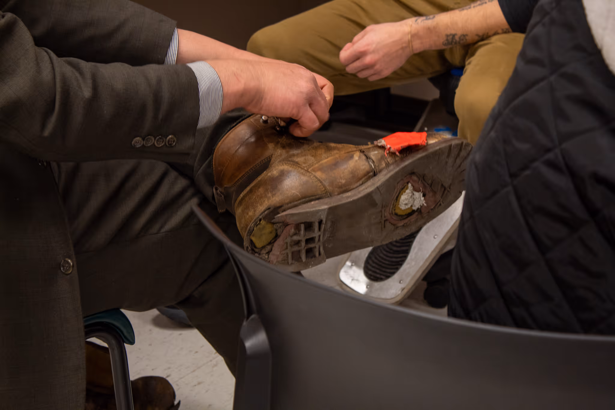 Close-up of a person repairing a worn brown leather boot with visible holes and patches on the sole and toe area.