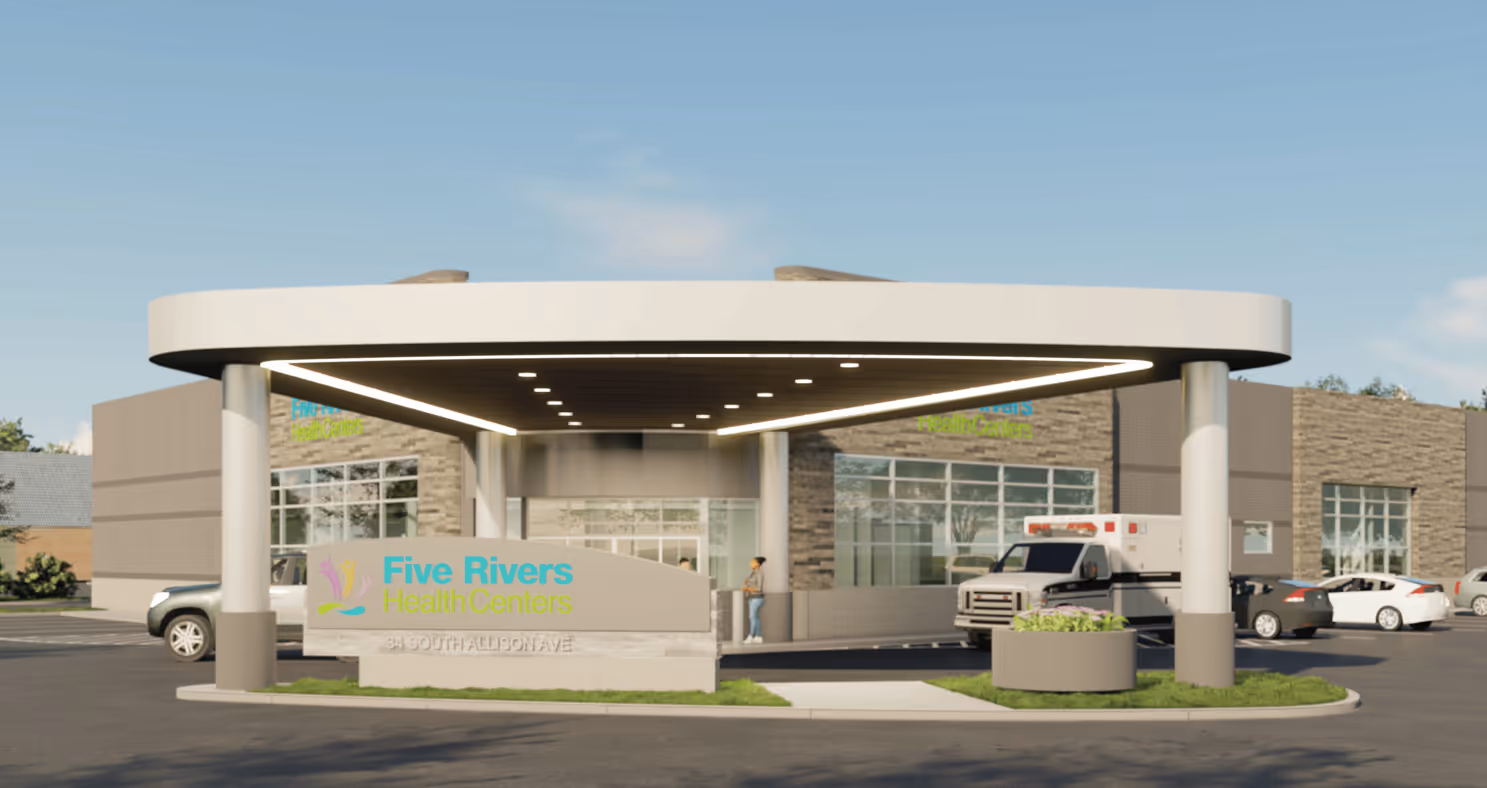 Entrance of Five Rivers Health Centers with a canopy, an ambulance, parked cars, and a person standing near the building.