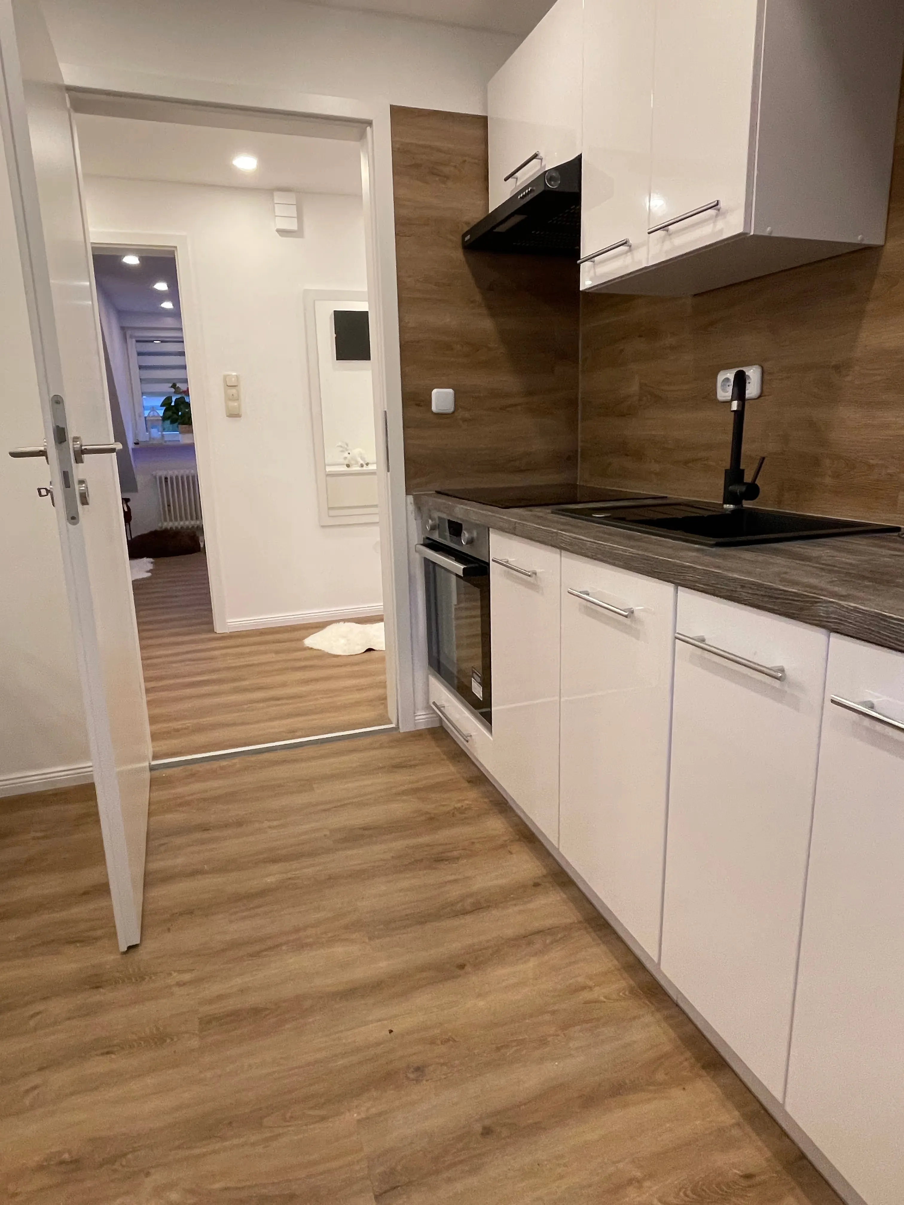 Moderne Küche mit weißen Schränken, Holzboden und Holzrückwand mit integriertem Herd und Spüle.