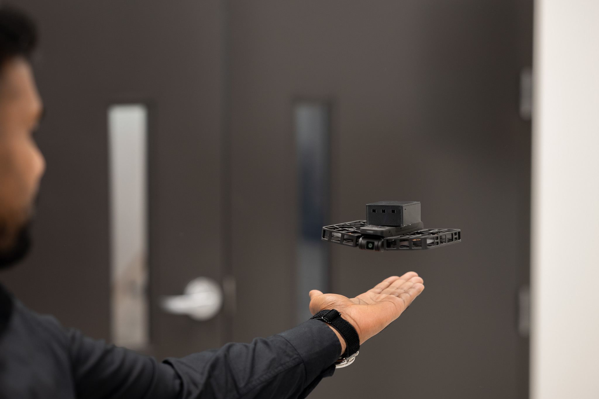 A Swarmnet communication payload hovering above a person's palm indoors, showcasing the compact device designed to attach to third-party drones.