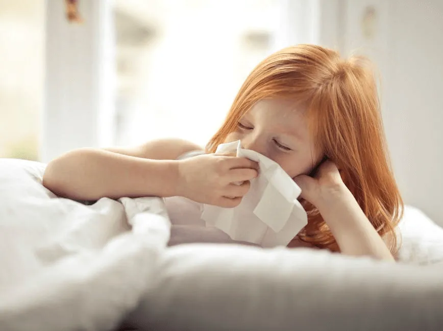 A little girl wipes her nose with a tissue, suffering from a summertime cold - her mom needs to know when to get care from the best pediatric doctor in East Brunswick, NJ