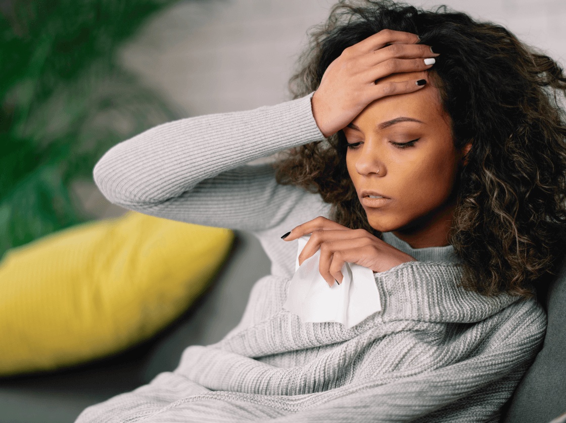 Woman resting on a couch with a headache and tissue needs prompt care through same-day sick visits in East Brunswick for sudden illness or symptoms.