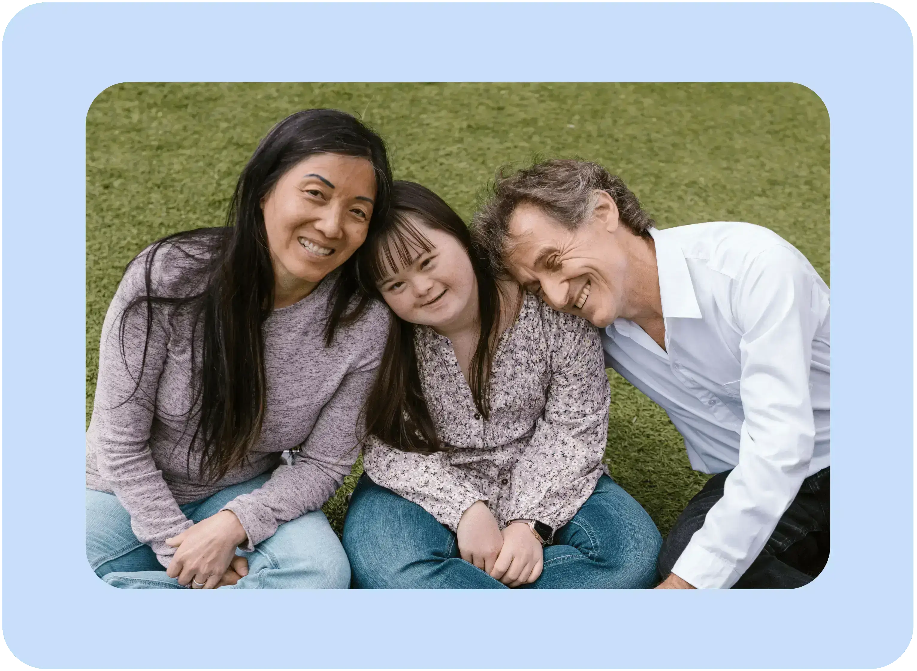 A smiling family sitting closely together on the grass, showing love and support connected through the spendAble disability money management app.