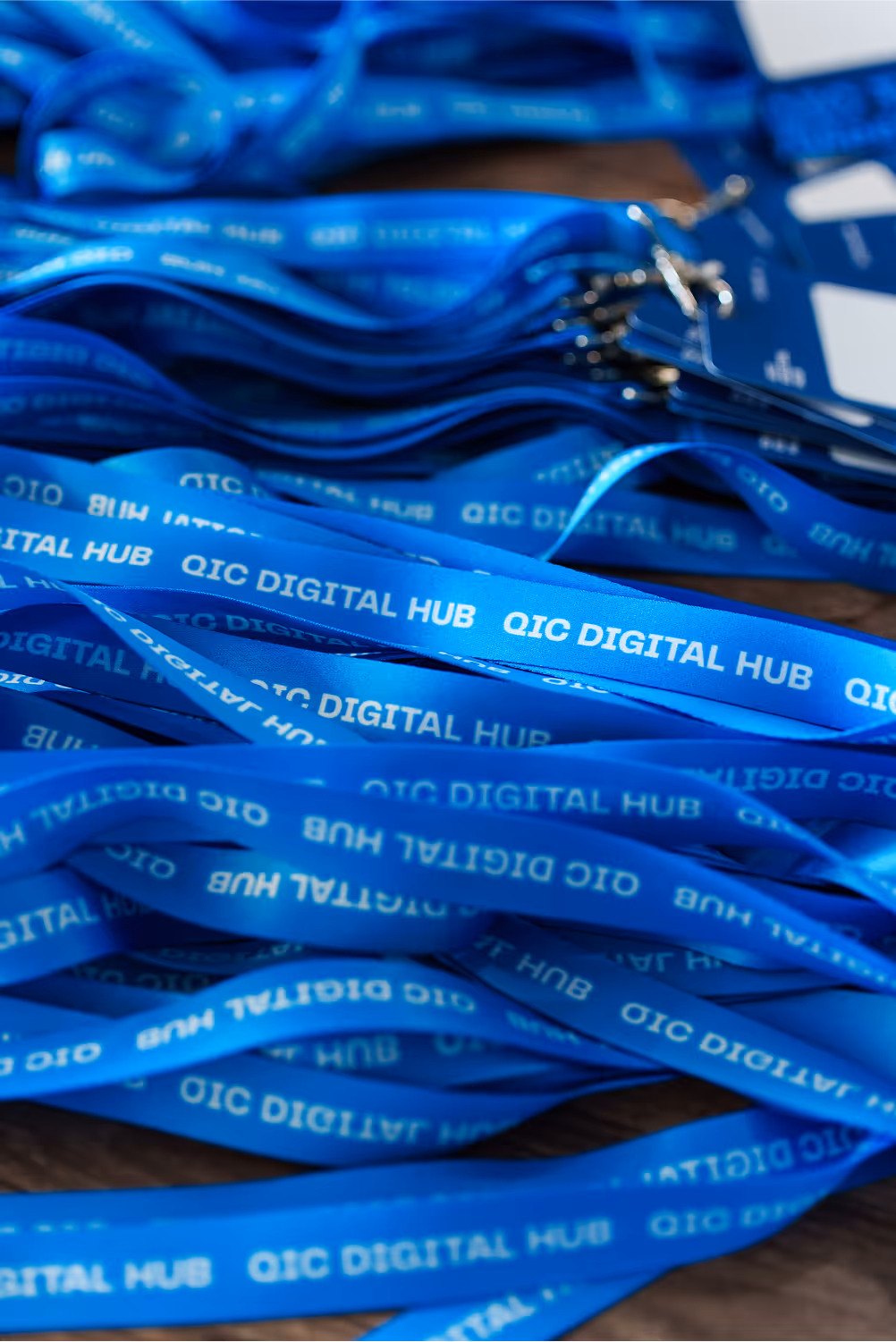 Pile of blue lanyards with white text reading 'QIC DIGITAL HUB' on a wooden surface.
