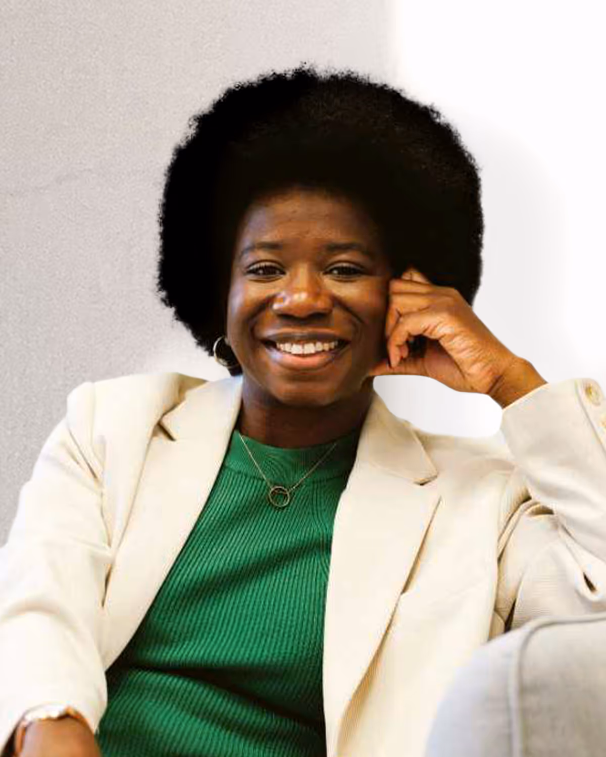 Smiling woman with afro hairstyle wearing a green top and cream blazer, resting her head on one hand.