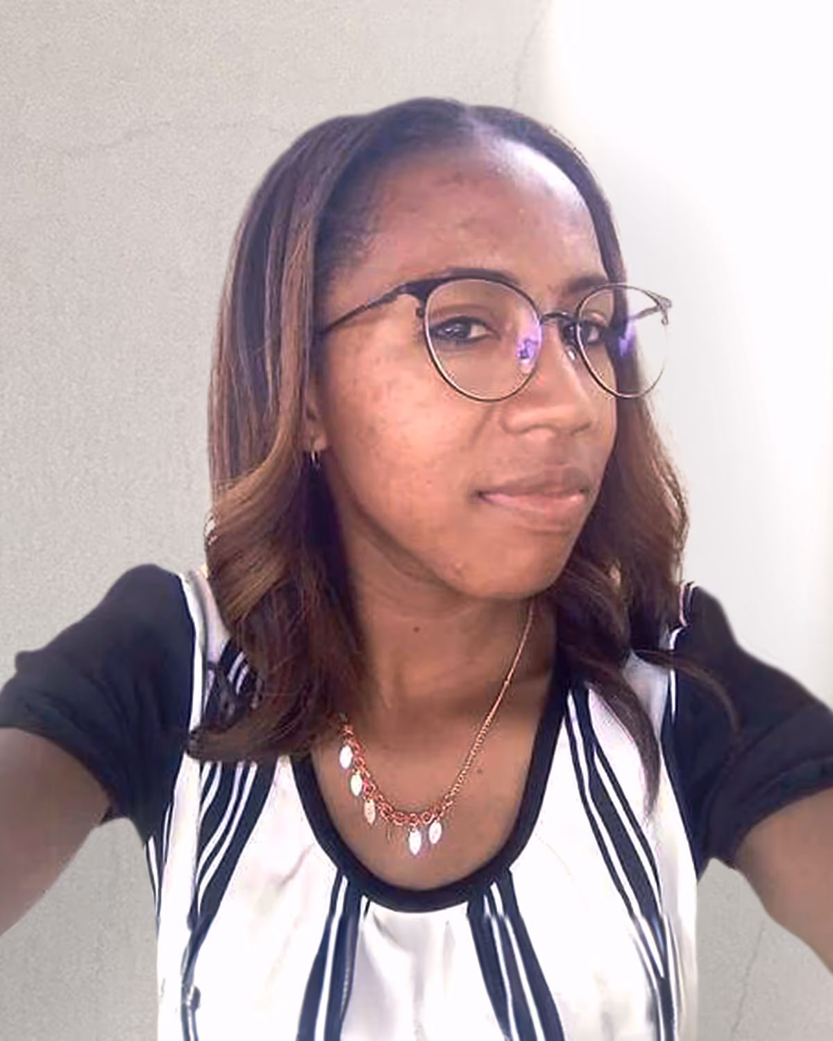 Young woman with glasses and shoulder-length hair wearing a striped white and black top and a gold necklace.