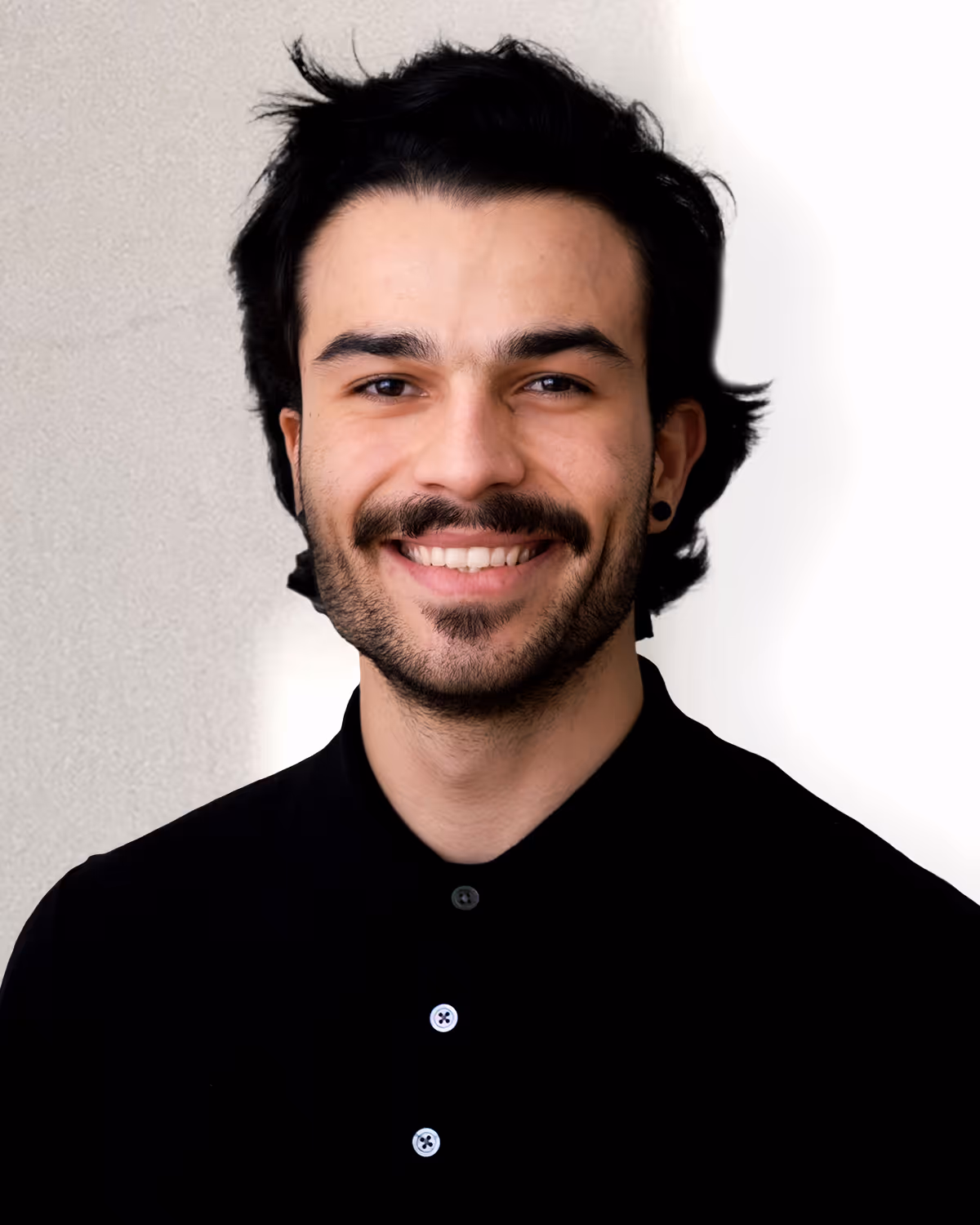 Smiling young man with dark hair, mustache, and beard wearing a black collared shirt against a light background.
