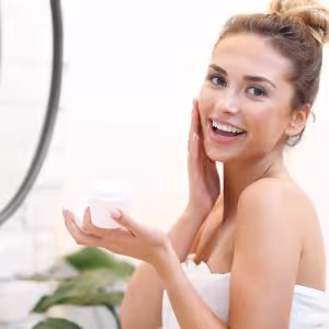 A smiling woman applying face moisturizer