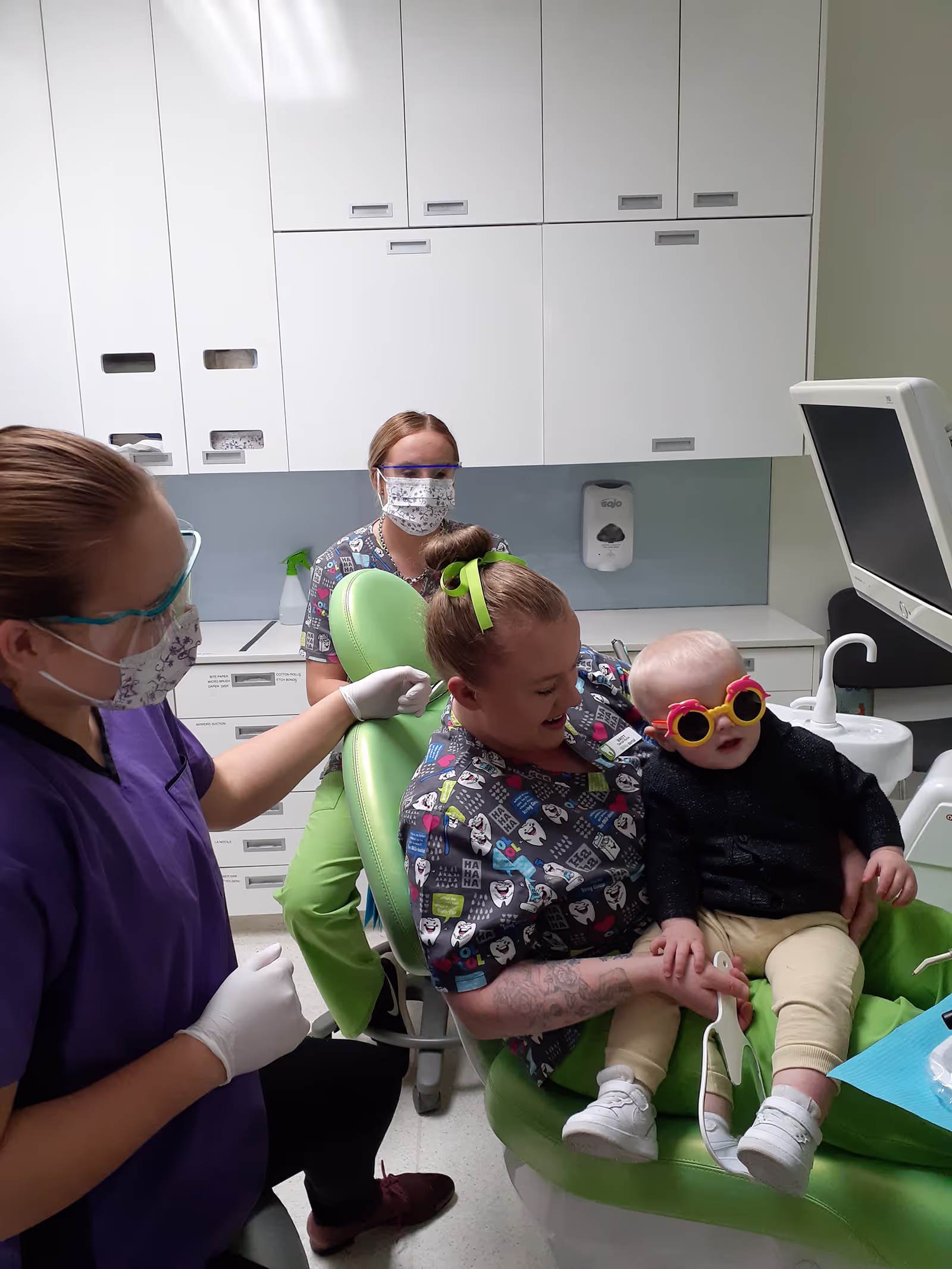 Woman sitting in dental chair with baby and dentists around
