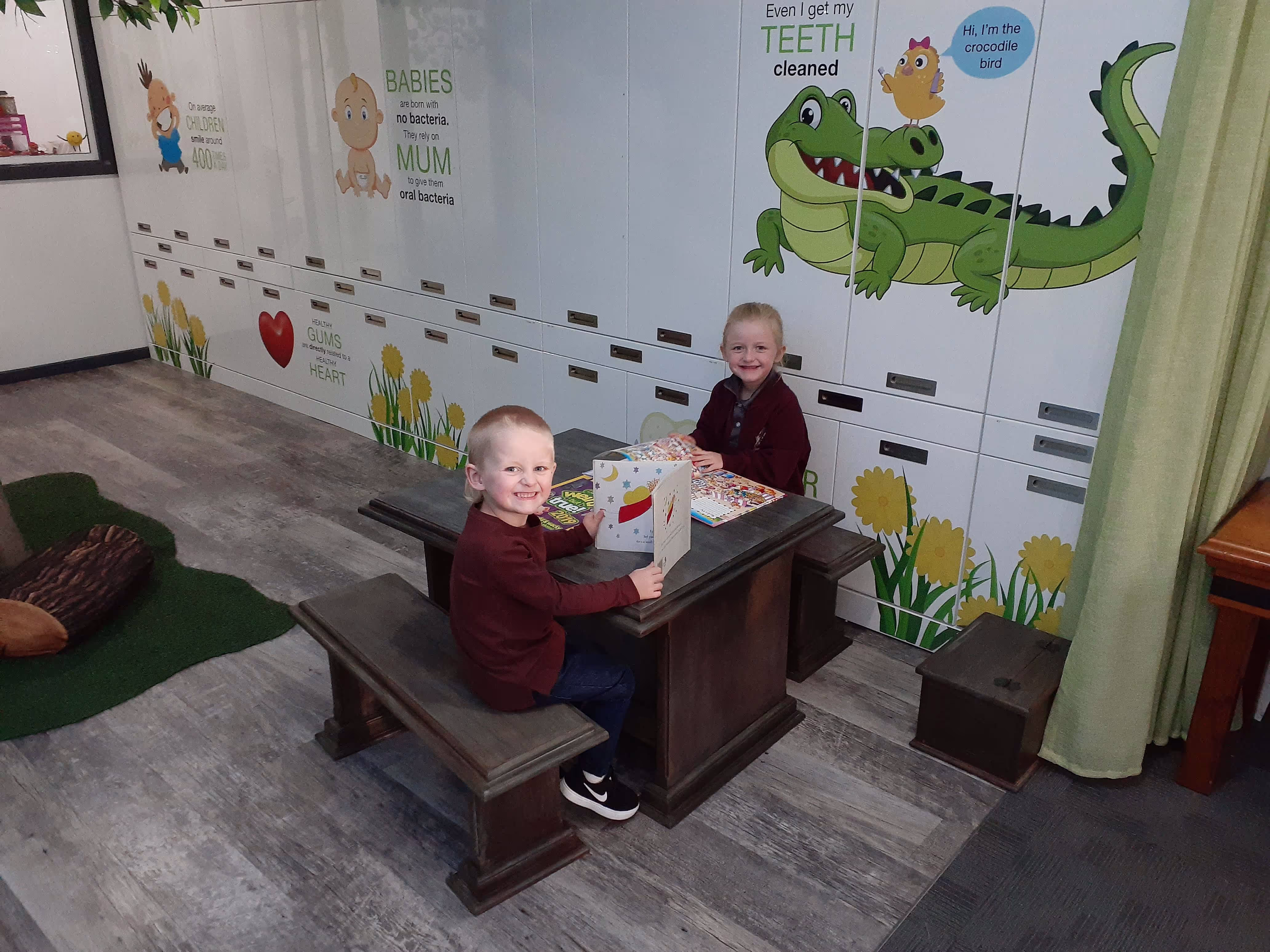 Two small children sitting at a table and chairs reading a book at the dentist