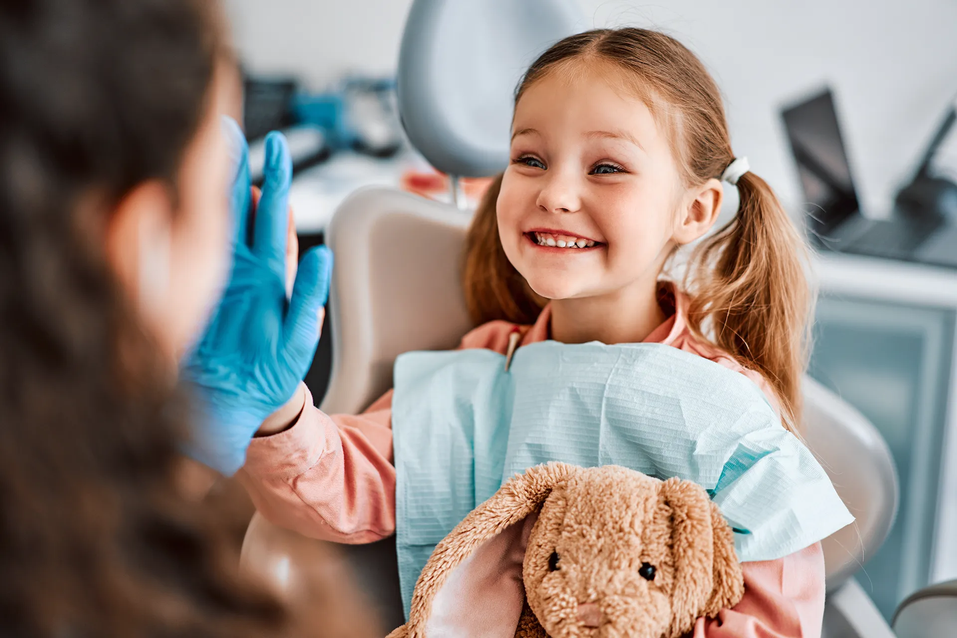 Child sitting in dental chair holding toy and smiling