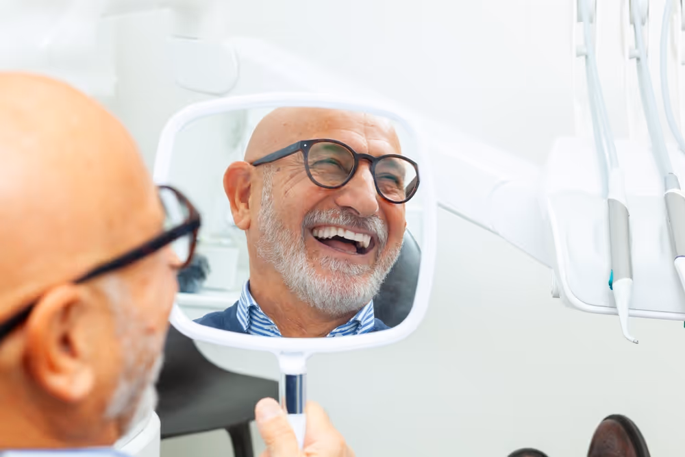 A man smiling and looking into a mirror at a dentist