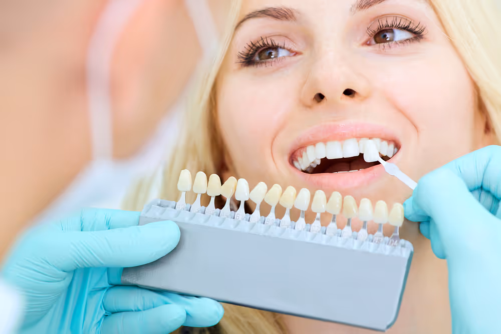 A dentist is comparing what colour to match with existing teeth of a woman patient 