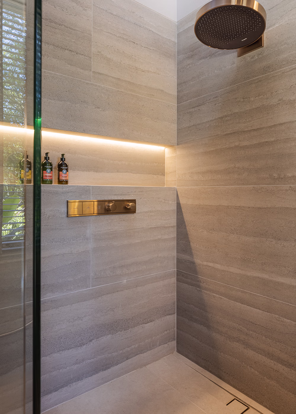 Ducha moderna con paredes de porcelanato gris y cabezal de ducha redondo de metal dorado.