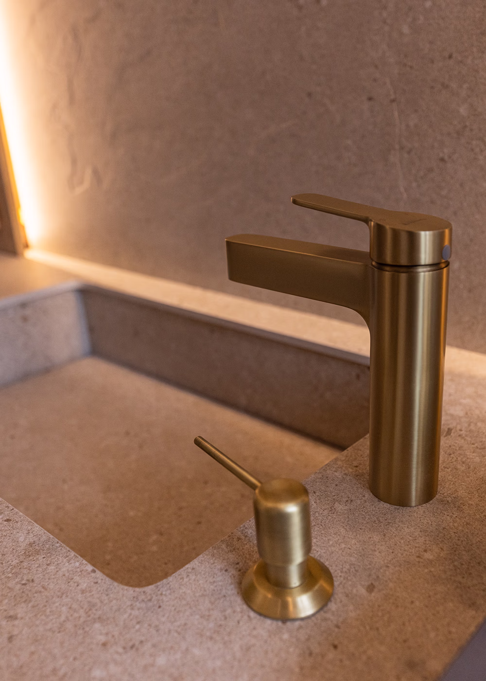 Grifo y dispensador de jabón dorado instalados en un lavabo de piedra beige.