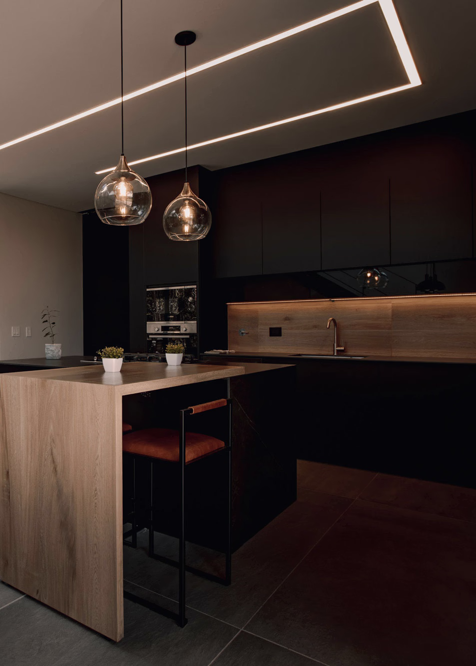 Lavabo moderno con mueble de madera, grifería dorada y jarrón con ramas secas sobre la encimera.