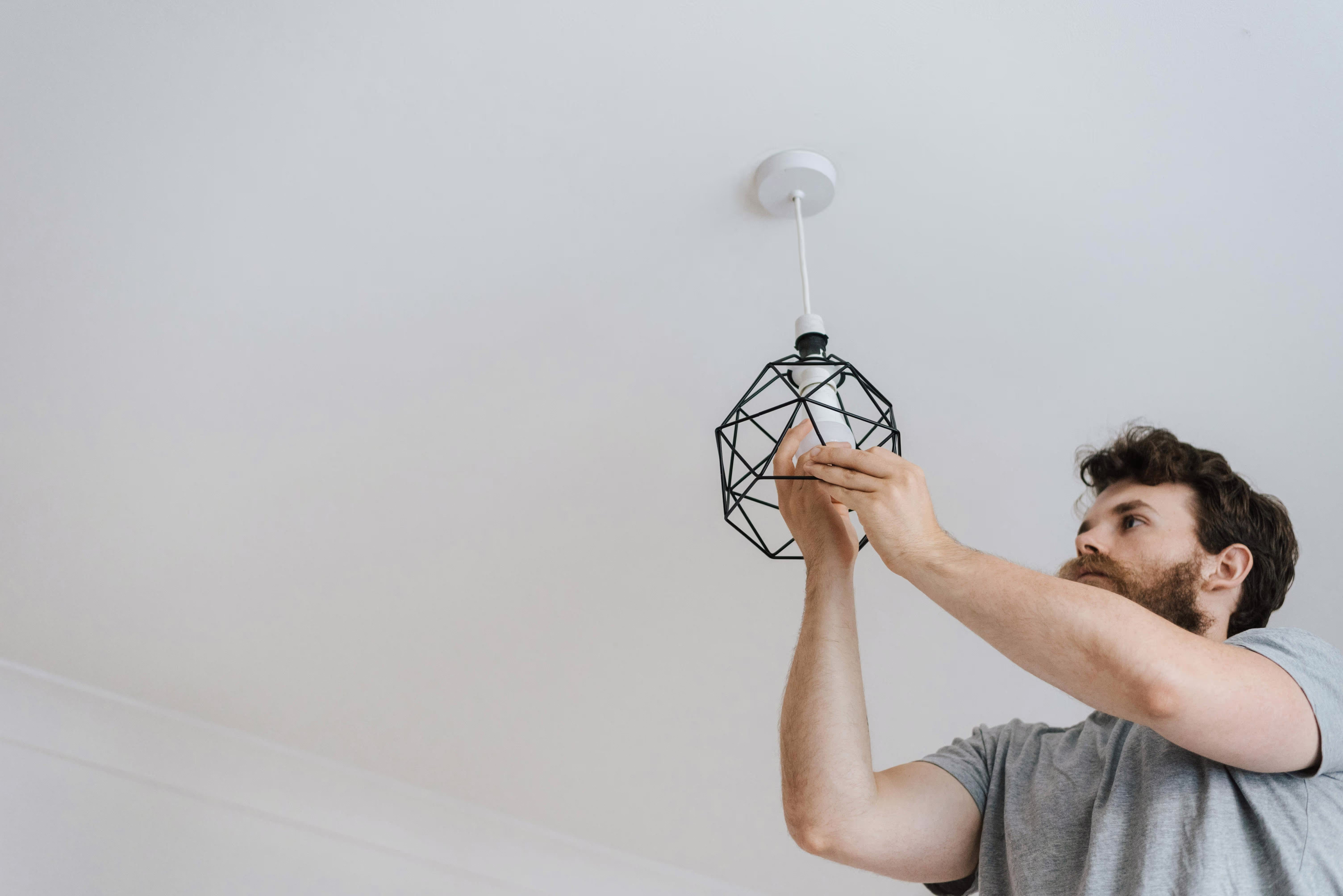 Man fixing the lightbulb on a black hanging ceiling light